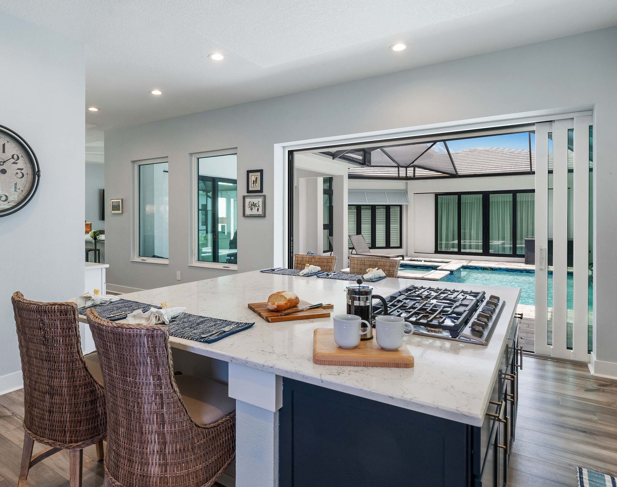 Deziner Tonie Interiors kitchen and island with built-in stove and seating looking out to lanai patio with pool in Loxahatchee Groves, FL.